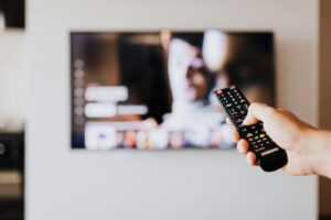 Person using a TV remote control with a blurred television screen in the background.