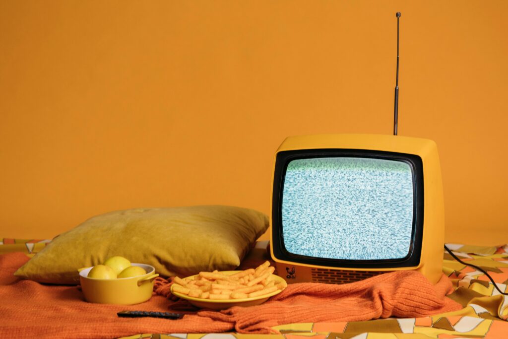 A vintage yellow TV with static, surrounded by fries, apples, and a cozy pillow setup.